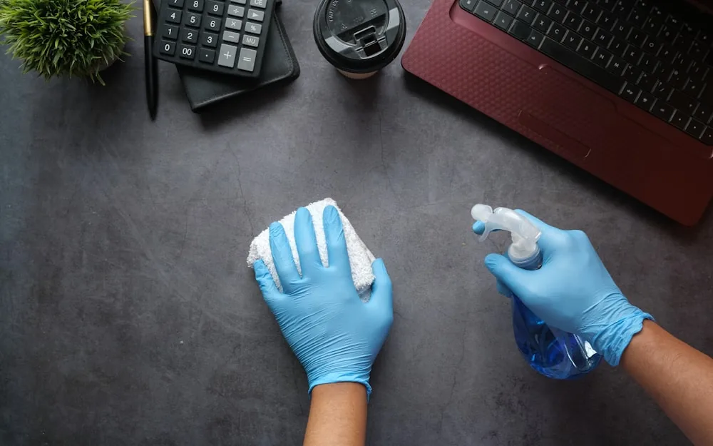 A gloved hand cleaning an office desk and keyboard.