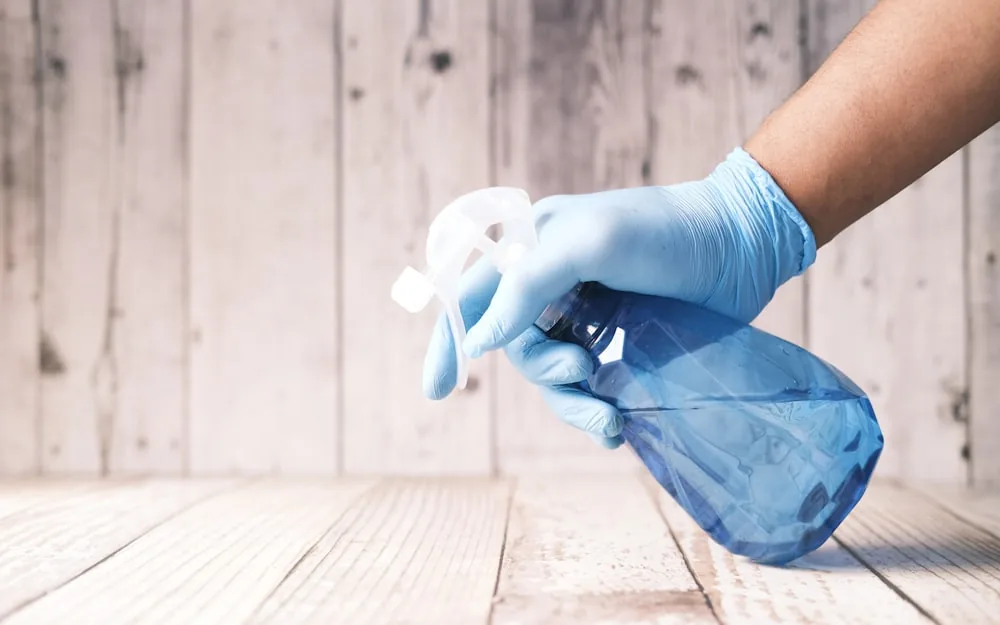 A gloved hand holding a spray bottle while deep cleaning a surface.