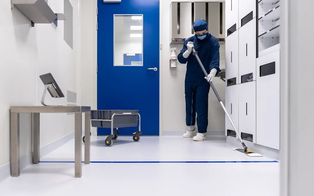 A cleaning operative mopping the floor of a commercial corridor with a wet floor sign.